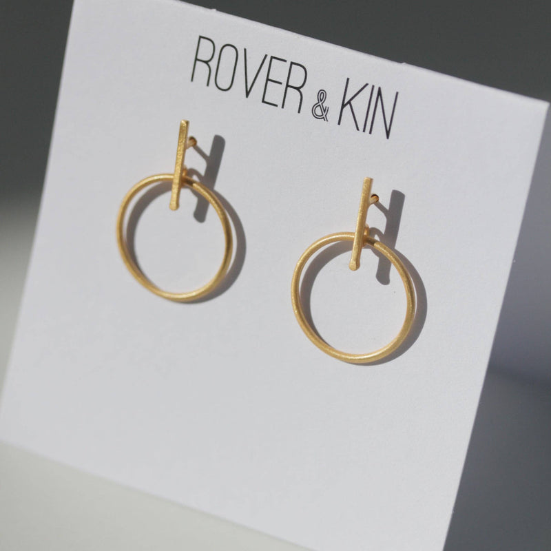 The Luxe Gold Outline Earrings in their folded paper packaging.