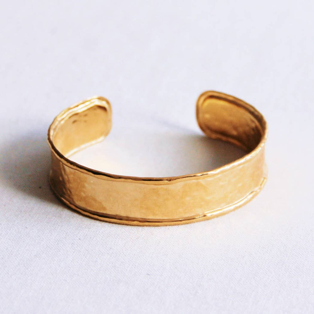 A wide gold stainless steel bangle bracelet with a hammered texture and raised edges.