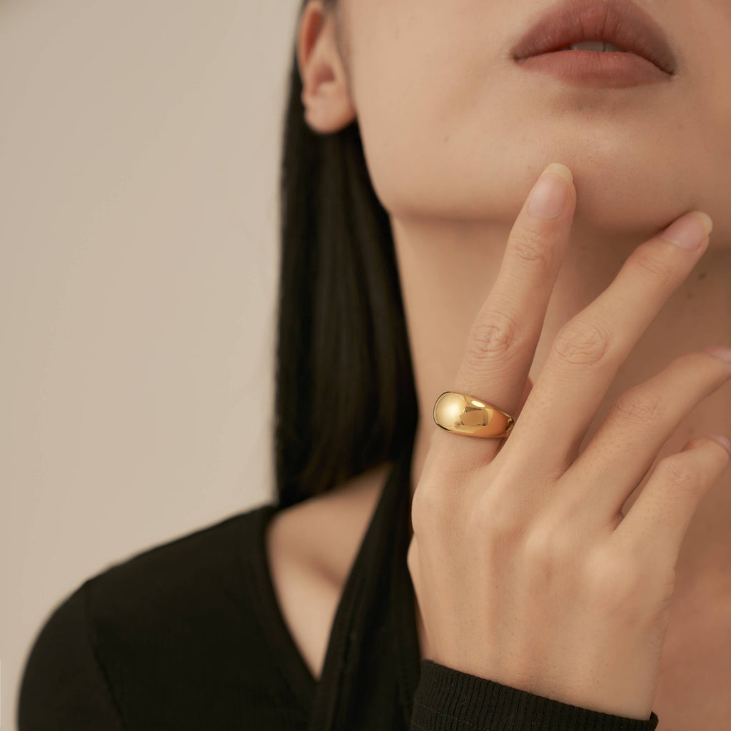 A person wearing a glossy gold plated stainless steel ring that has a wide round shape.