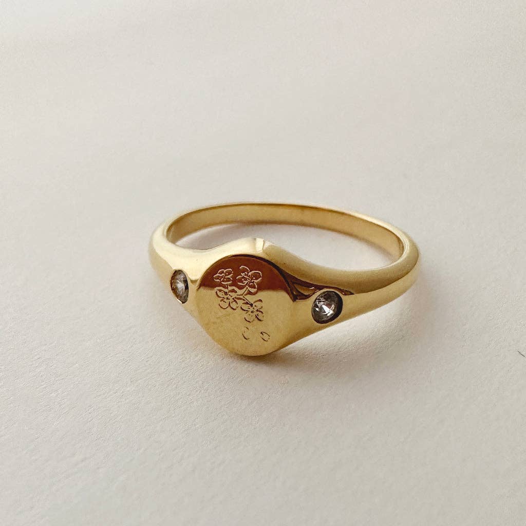 A gold plated signet ring engraved wi flowers with an embedded crystal on either side.