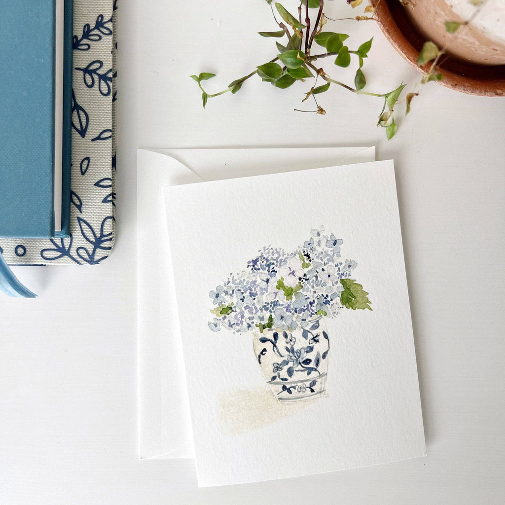 A Hydrangea Bouquet Notecard on a desk next to a notebook and a potted plant.