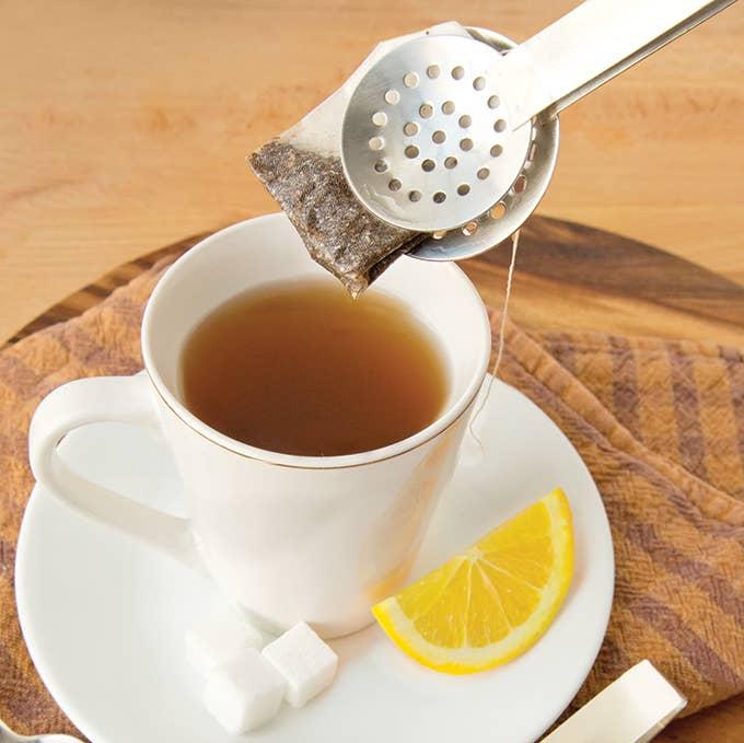 A Tea Bag Squeezer holding a tea bag over a cup of tea.