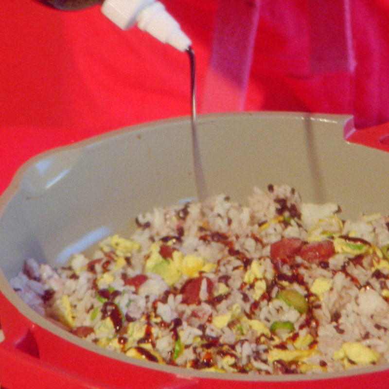 A person squeezing some Woon Stir Fry Sauce into a bowl of stir fry.