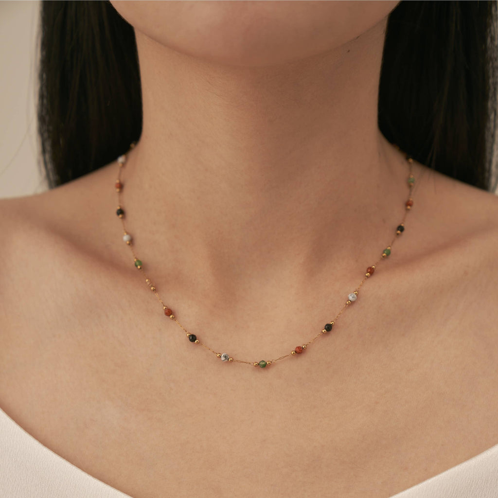 A person wearing a gold plated stainless steel chain necklace with orange, black, white, and green agate stones interspersed equally along the chain.