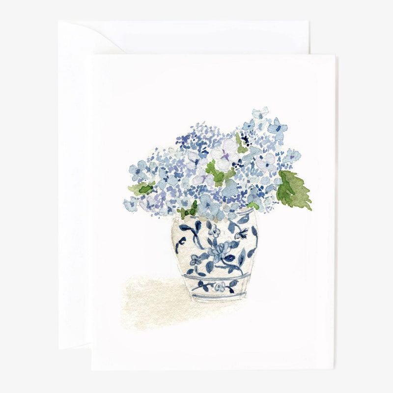 A white note card watercolor illustrated with pale blue hydrangeas in a white and blue vase and a white envelope behind.