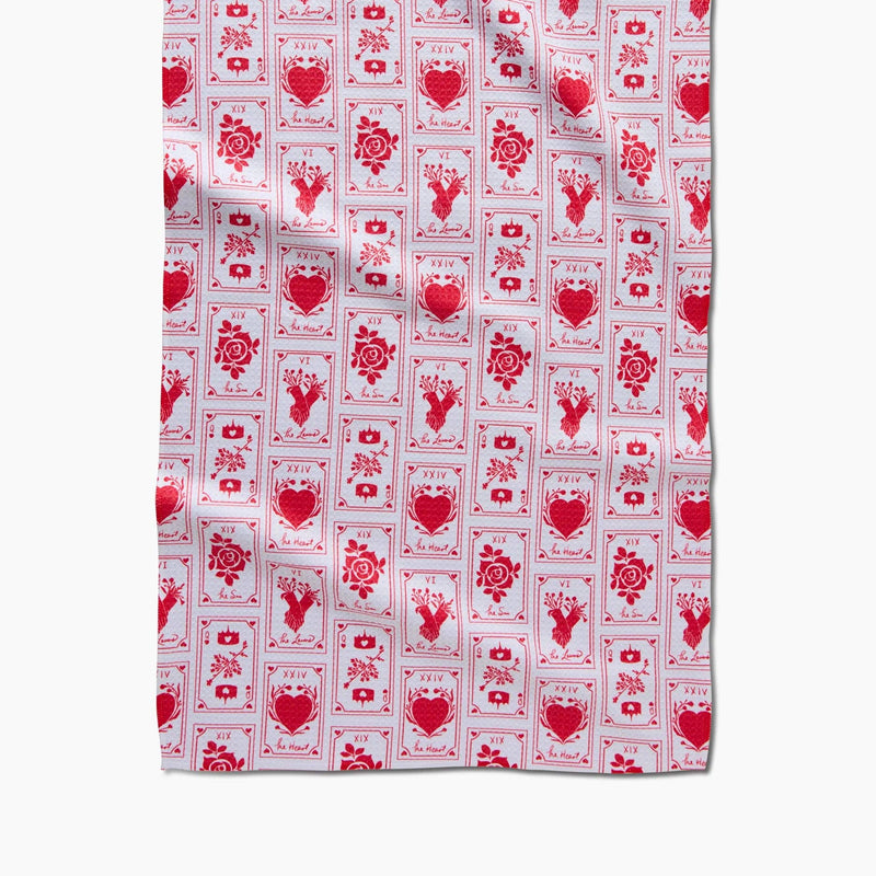 A white tea towel patterned with red cards such as The Lovers, the Queen of Hearts, and the Sun.