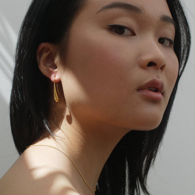 A person wearing the Luxe Gold Droplet Earrings with a ray of sun hitting the ear.