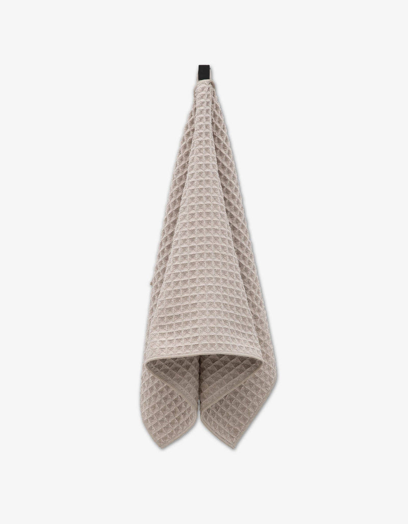 A cream waffle texture hand towel hanging from an attached fabric loop.