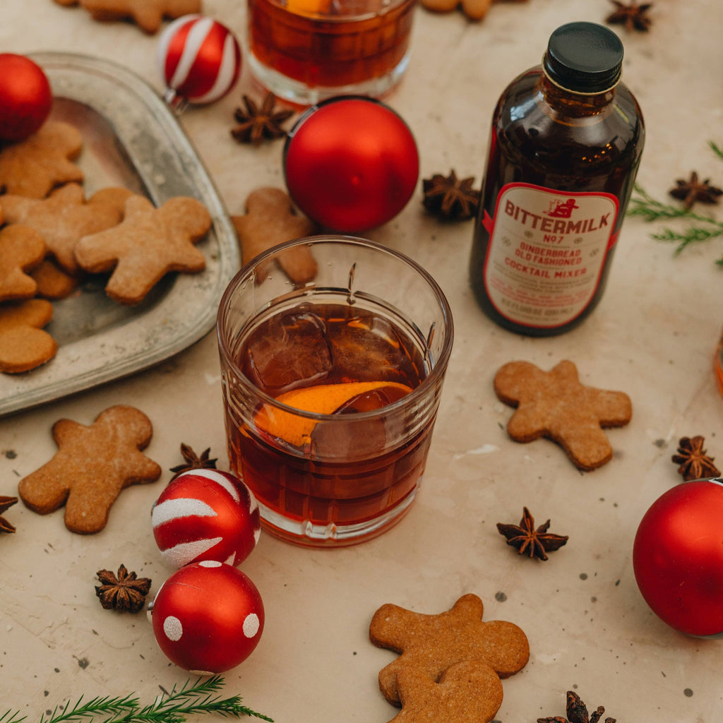 A glass of No.7 Gingerbread old Fashioned surrounded by gingerbread cookies, ornaments, star anise, and a bottle of No. 7.