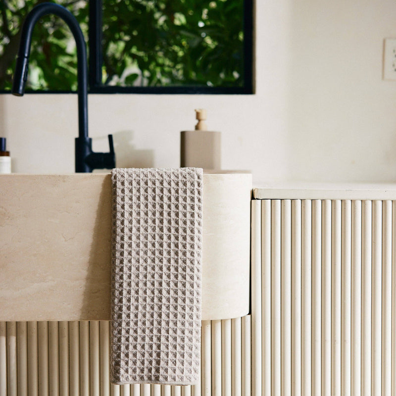 A Taupe Waffle Hand Towel hanging off a kitchen sink.