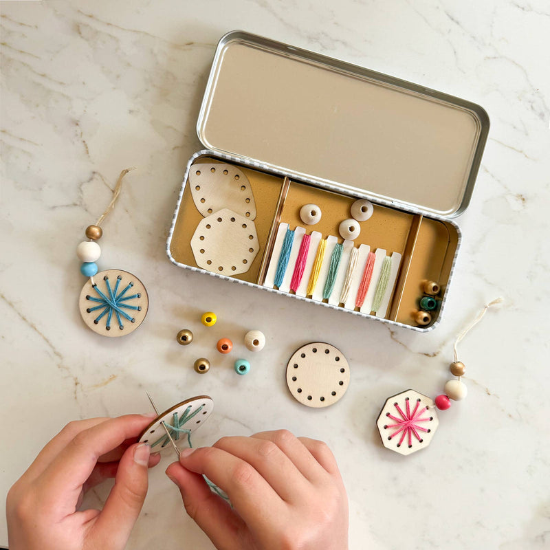 A pair of hands using the needle to thread embroidery thread through a wooden ornament.