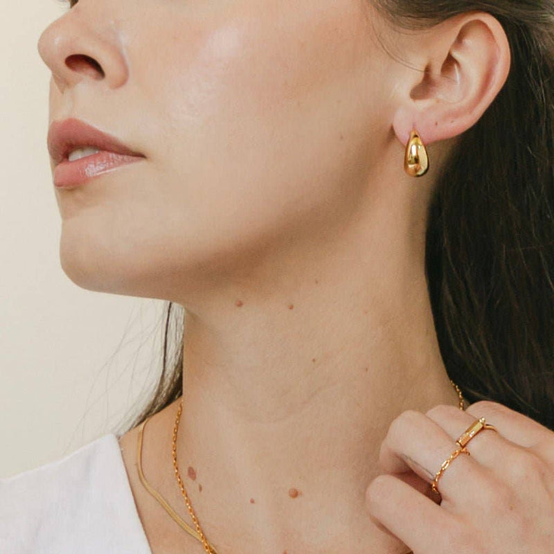 A person looking to their right while wearing the Dumpling Hoops in Gold.