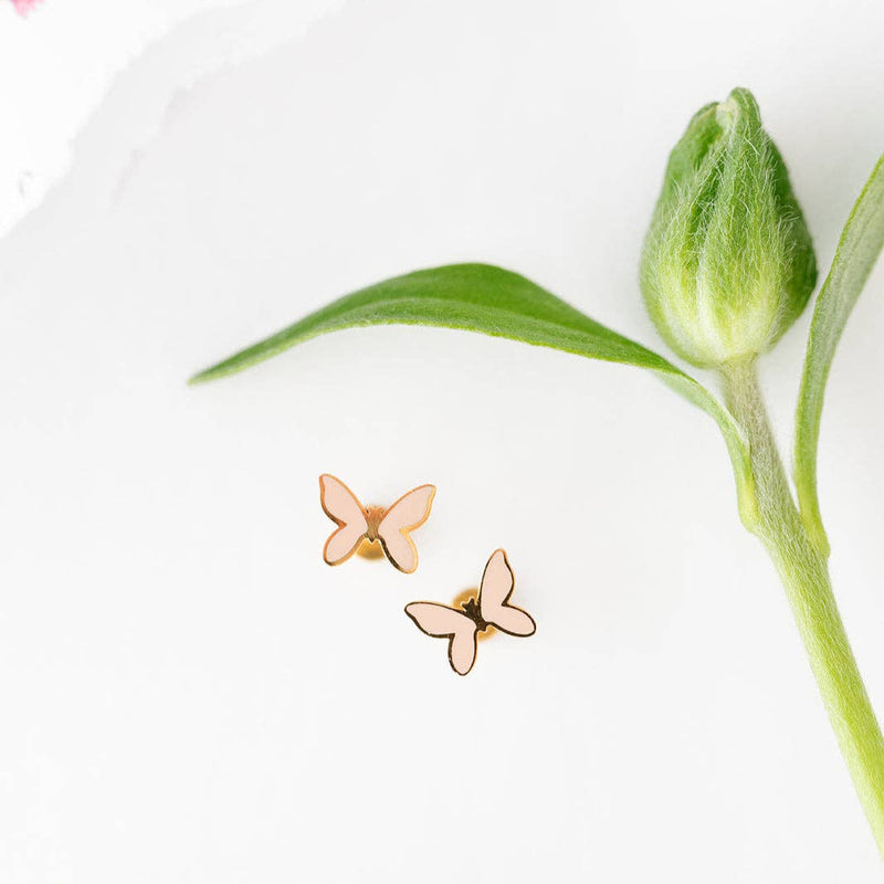 A pair of blush Butterfly Earrings next to a fuzzy flower stem.