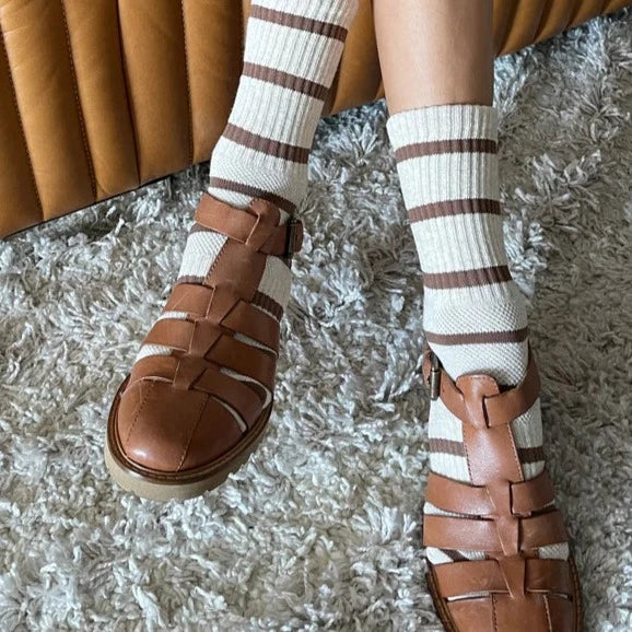 A person crossing their legs while wearing the Boyfriend Socks with brown leather sandals.