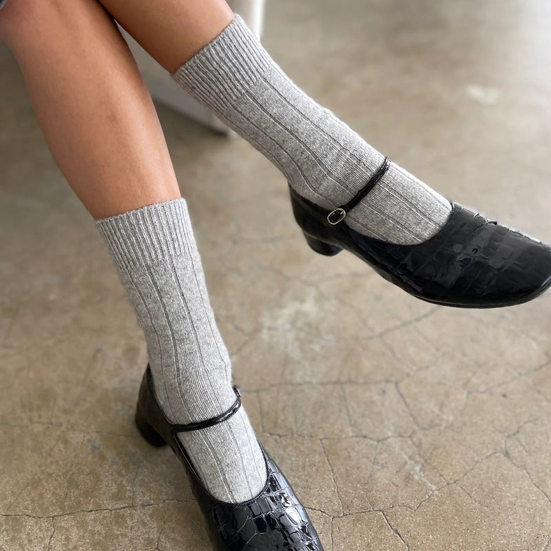 A person wearing the Cashmere Classic Socks in Grey Melange with black snake print mary janes.