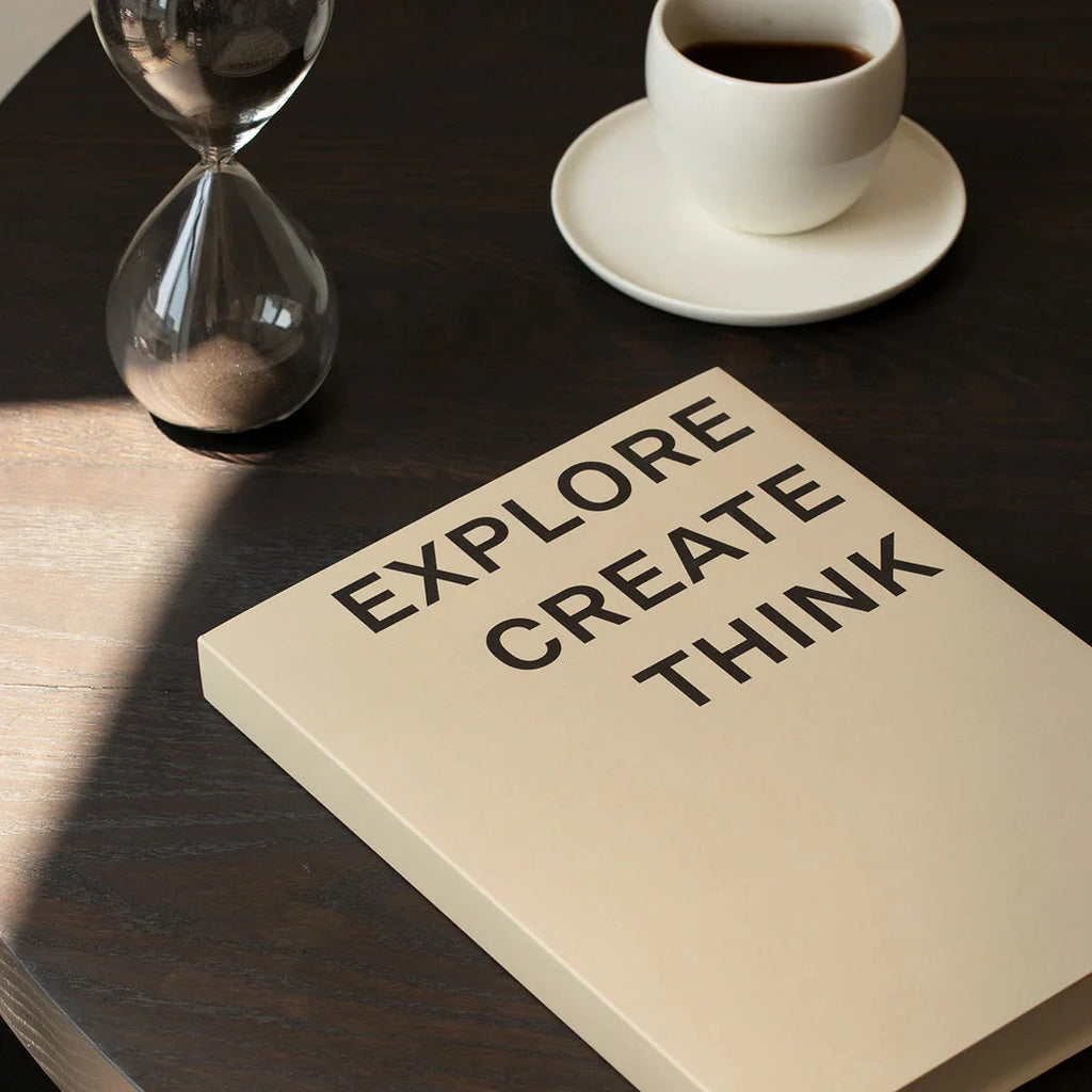 A Quote Notebook resting on a wooden table next to a cup of coffee and an hourglass.