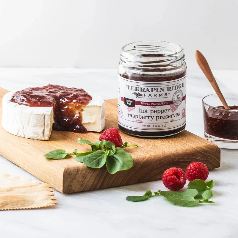 A charcuterie board with Hot Pepper Raspberry Preserves on a wheel of cheese.