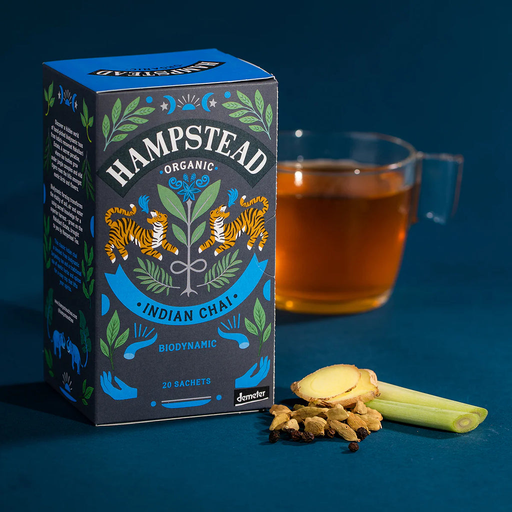 A box of Indian Chai next to a pile of chai ingredients and a freshly brewed cup of Indian Chai.