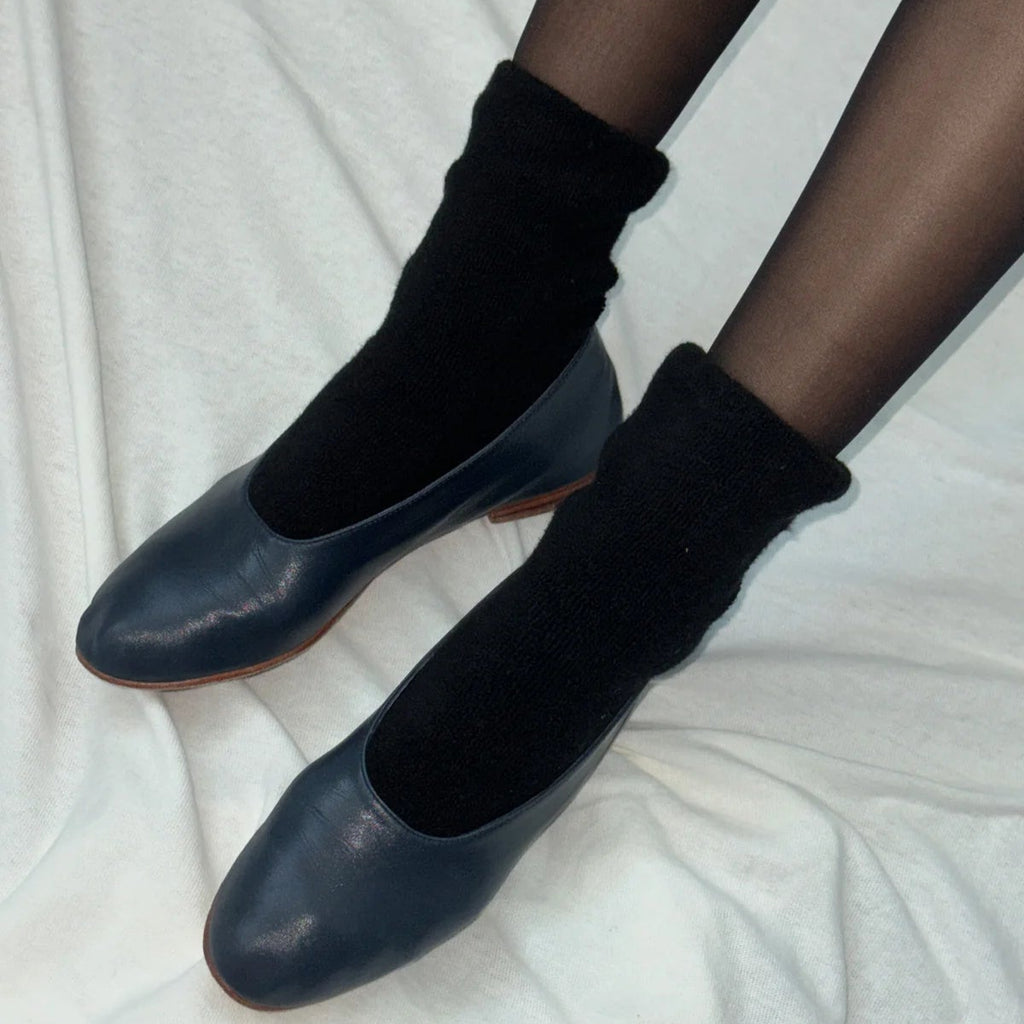 A person wearing the Cloud Socks in Jet Black with black ballet flats and black tights.