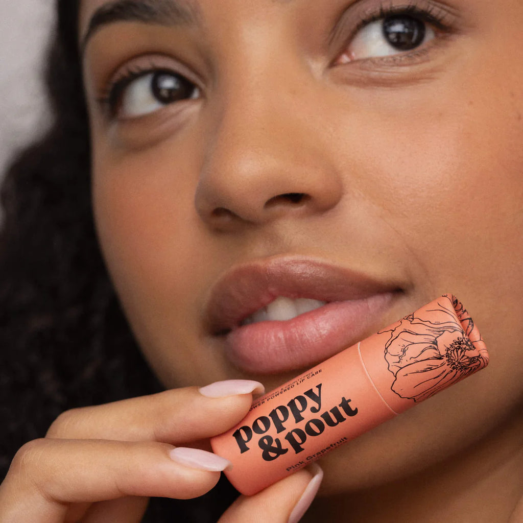 A person holding the Pink Grapefruit Lip Balm up to their lips.