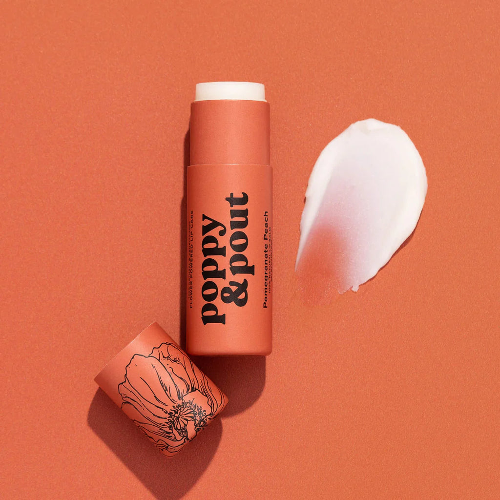 An open peach colored tube of Pomegranate Peach lip balm next to its lid and a swatch of the balm.