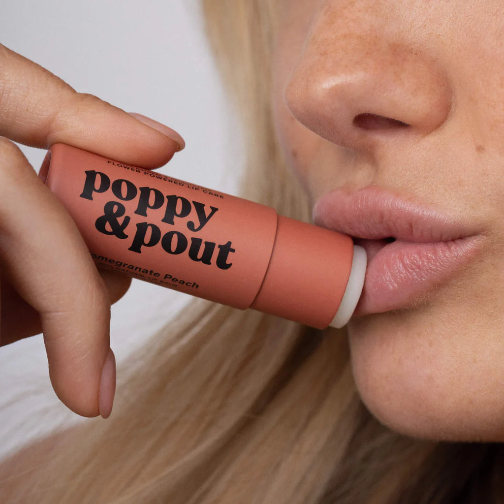 A person applying Pomegranate Peach Lip Balm to their lips.