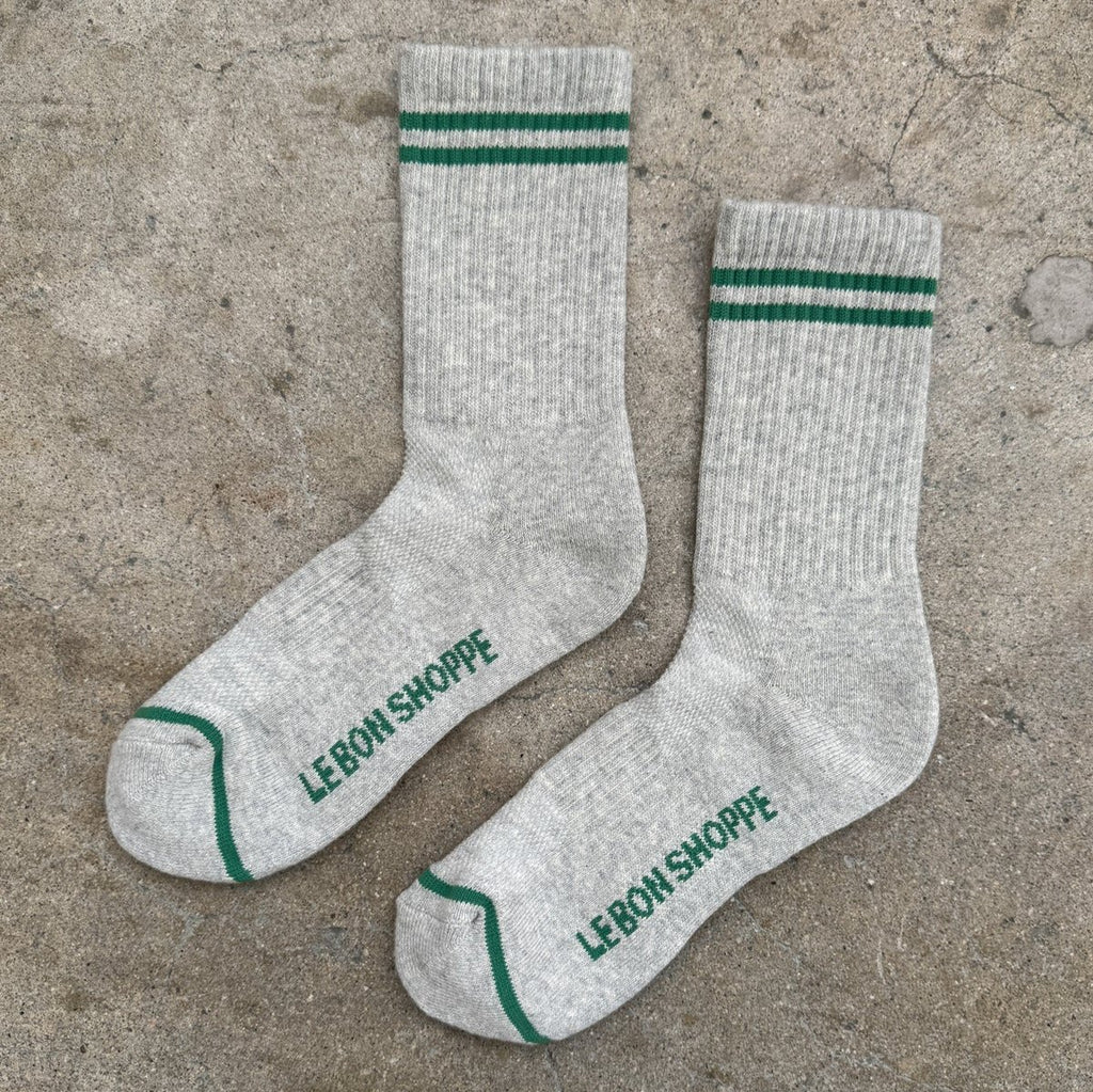 A pair of long light gray socks with green stripes above the ankle and at the toe.