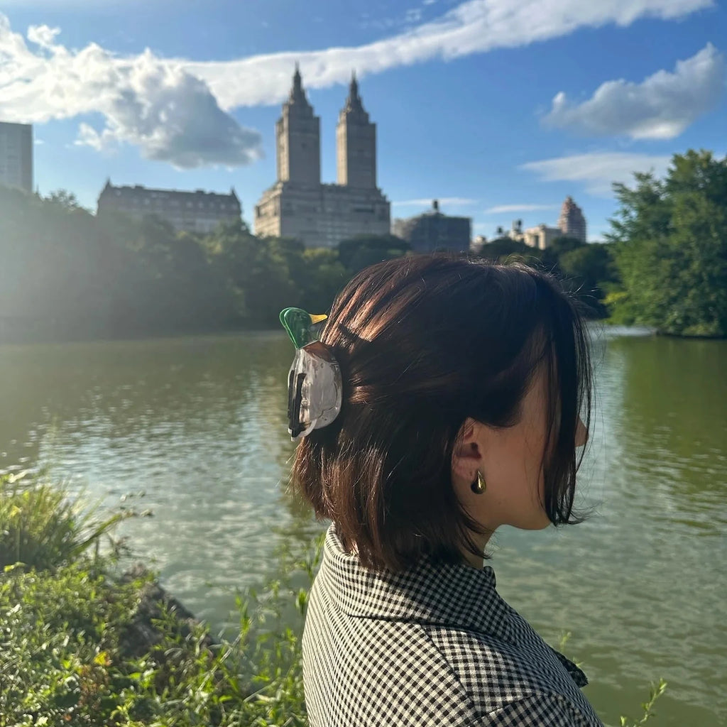 A person wearing the Mallard Duck Claw Clip in a half-up hairstyle at a park's pond.