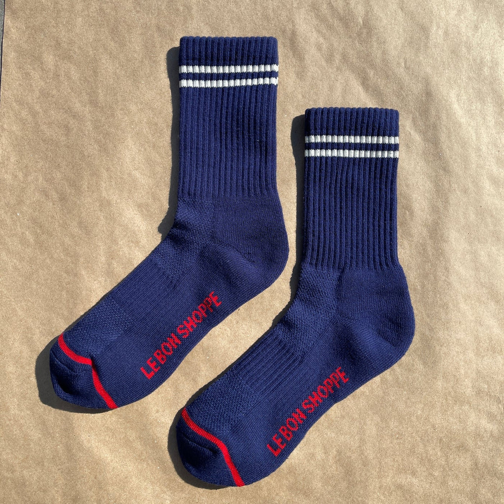 A pair of navy blue crew length socks with a red stripe at the toe and two white stripes above the ankle.