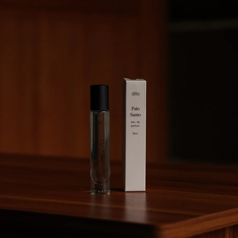 A glass vial of Travel Size Palo Santo next to its pale pink box packaging.