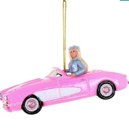 A blonde barbie driving a pink corvette with a gold cord attached.