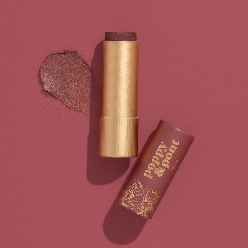 An open brick pink Roxie Lip Tint with a gold tube next to its cap and a swatch against a similarly colored background.