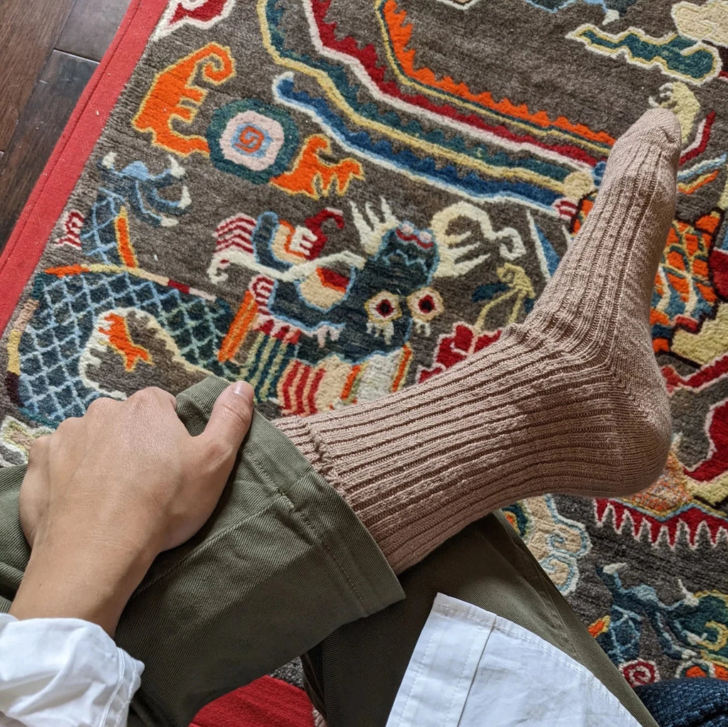 A person with their legs crossed wearing the Cottage Socks in Toffee.