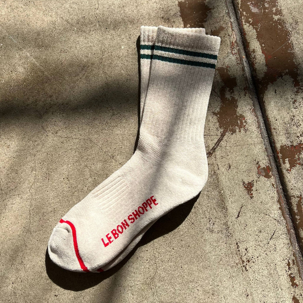 A pair of oatmeal colored Boyfriend Socks with two black stripes on the top and one red stripe at the toes.