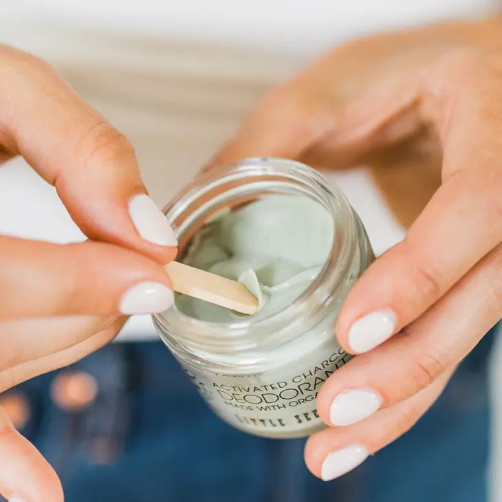 A pair of hands scooping a bit of deodorant cream with a popsicle stick.