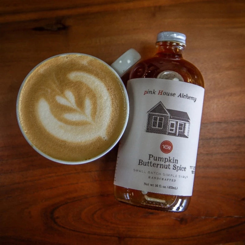 A bird's eye view of Pumpkin Butternut Spice Syrup on it's side next to a hot cappucino.